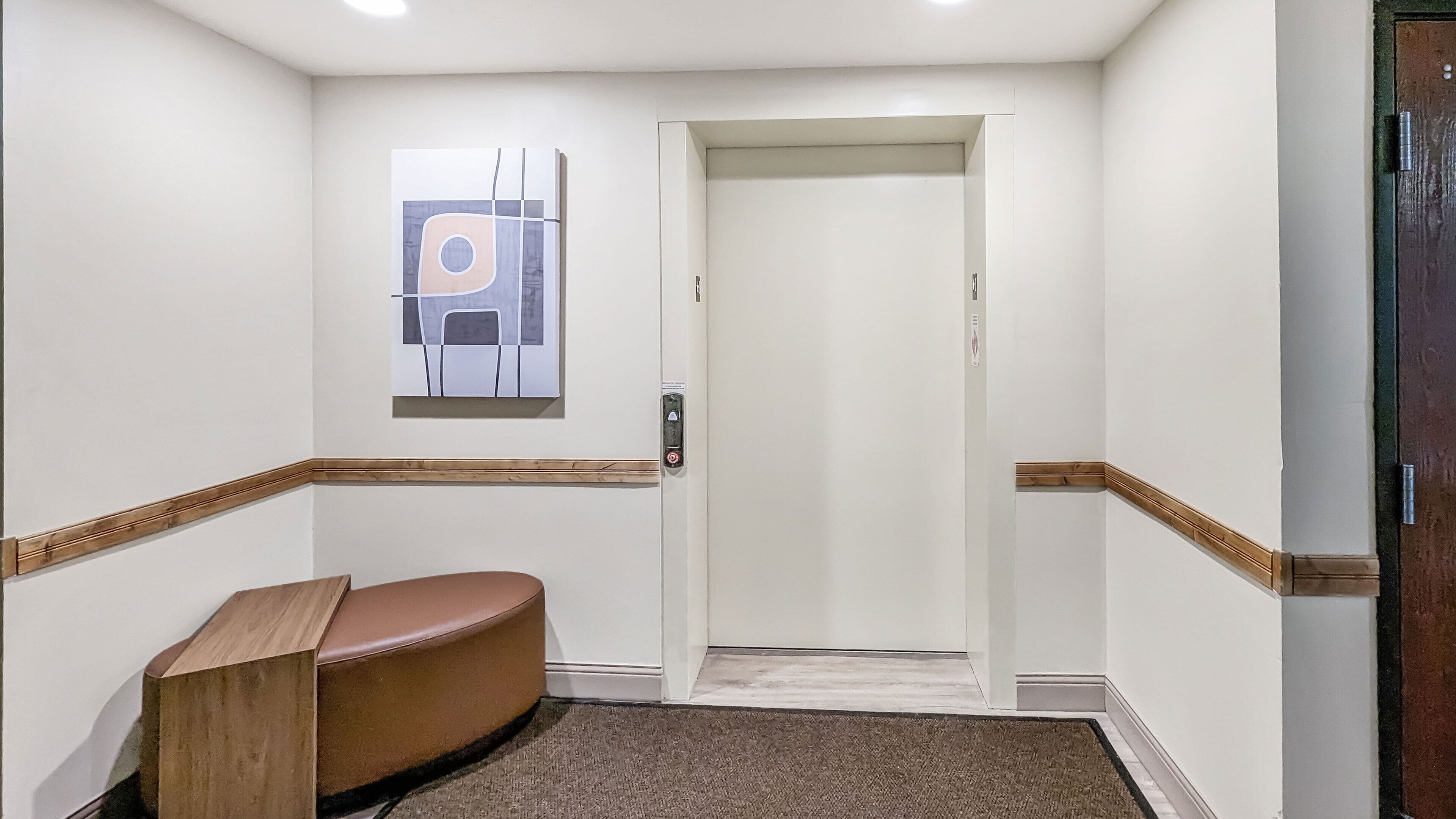 A hallway with a wooden bench, a door with a handle, and a wall-mounted light switch.