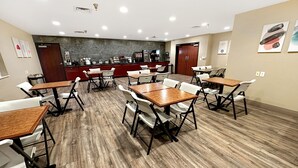Un espace repas avec plusieurs tables et chaises, une cuisine à l’arrière-plan et un mur en pierre.