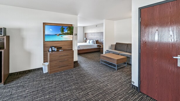 Une chambre d’hôtel avec un lit, un canapé, une commode en bois et un téléviseur fixé au mur.
