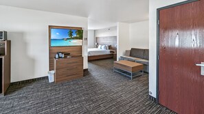 A hotel room with a bed, a sofa, a wooden dresser, and a television on the wall.