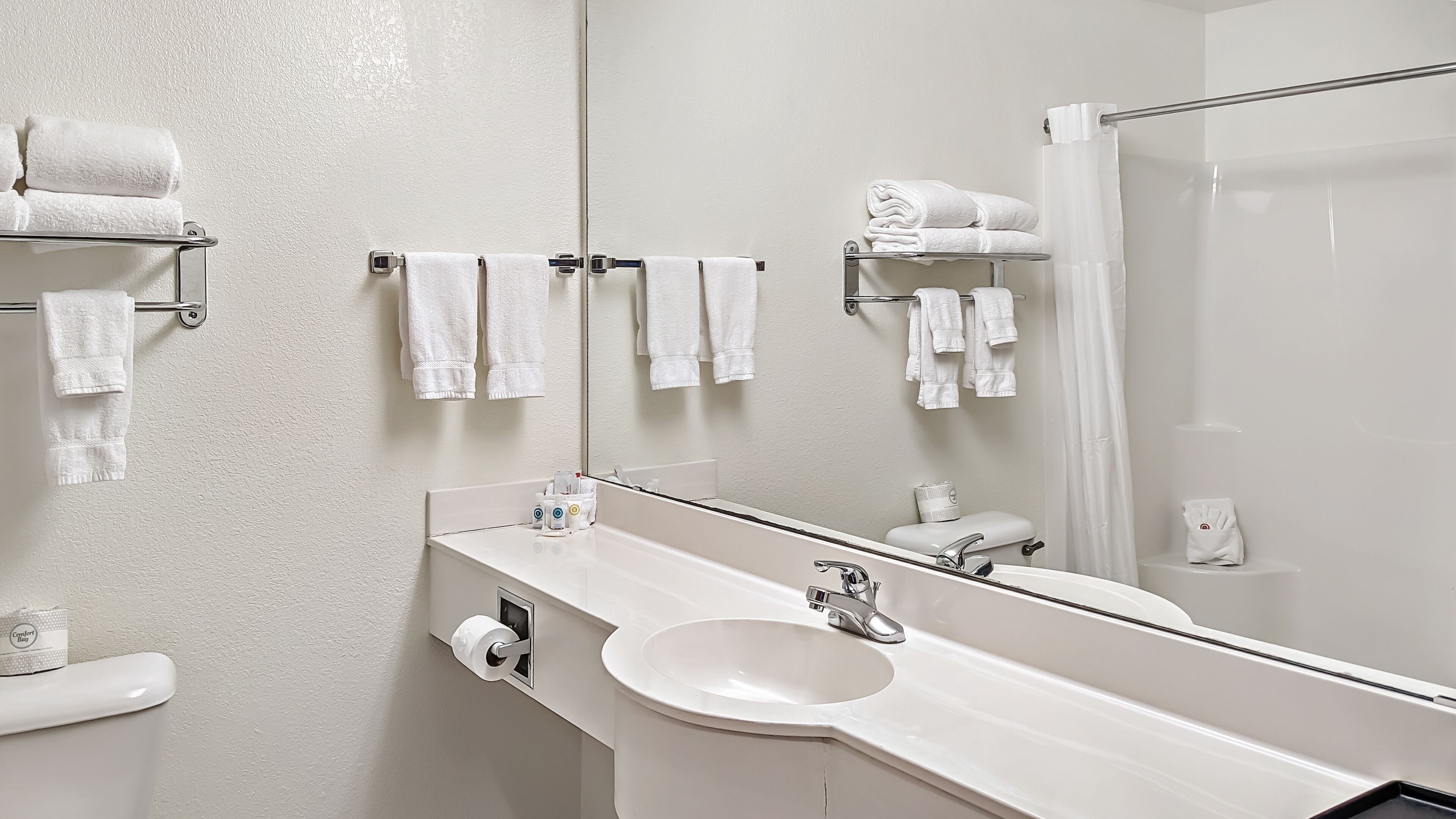A modern bathroom with a white sink, a large mirror, and multiple towel racks.