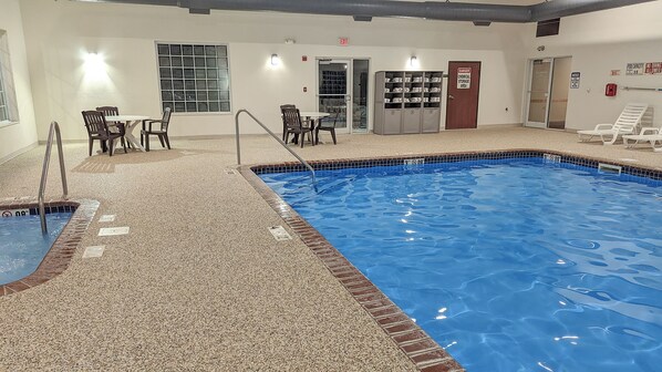 An indoor swimming pool with a tiled floor, a pool ladder, and a safety sign.