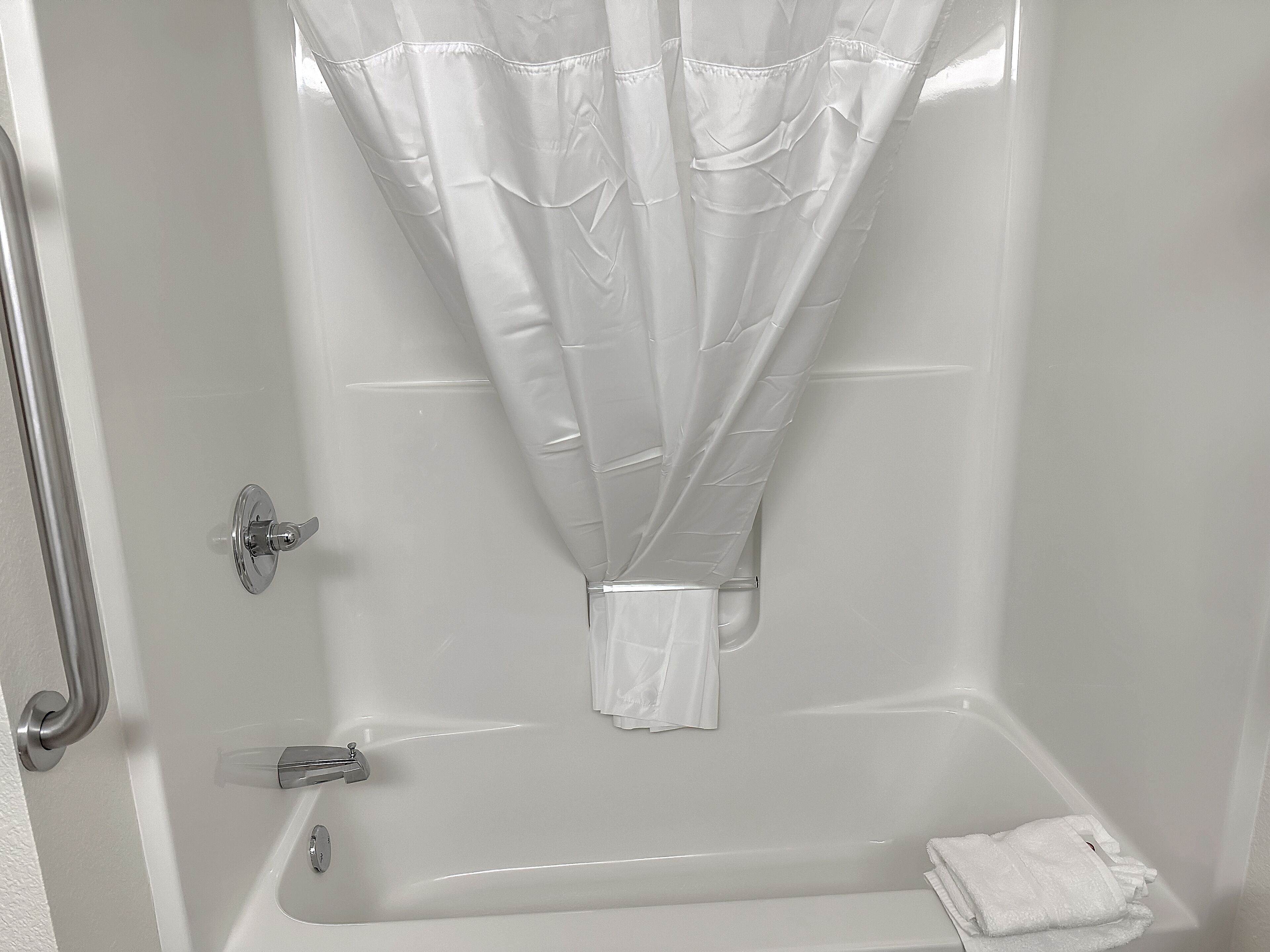 Una bañera blanca con cortina de ducha, toallero y barra de apoyo.