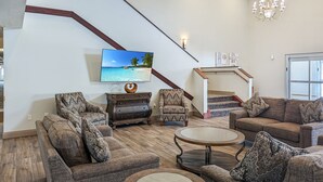 Un salon avec des canapés à motifs, une table basse, un téléviseur fixé au mur, un escalier offrant une vue dégagée et un lustre.
