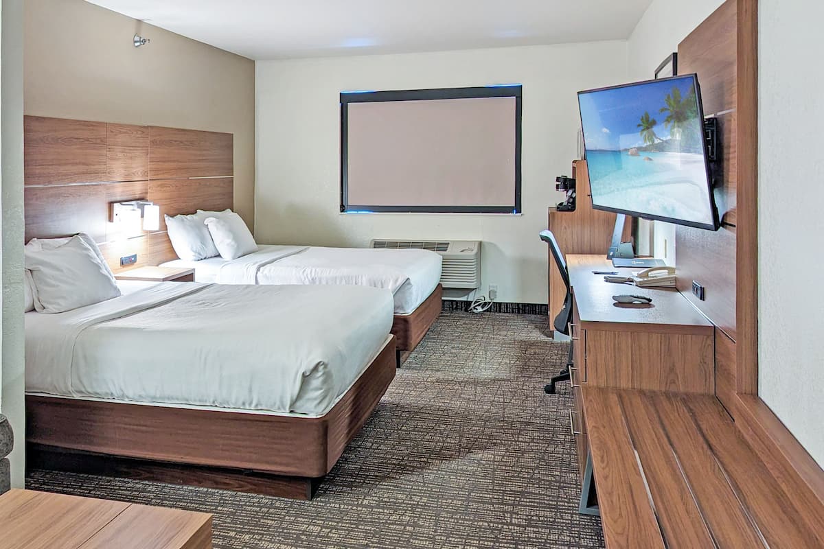 Een hotelkamer met twee bedden, een bureau, een televisie en een groot raam.