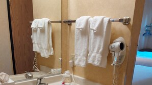 Une salle de bain équipée d’un lavabo, d’un miroir, d’un porte-serviettes, d’un sèche-cheveux et d’une poubelle.