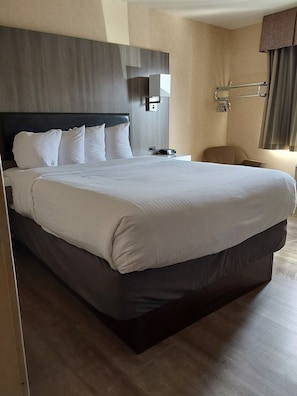 A neatly made bed with white linens, a dark headboard, and a bedside table with a lamp and a power outlet.