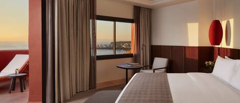 Habitación de hotel con una cama grande, una mesita pequeña, una silla y vista al mar.