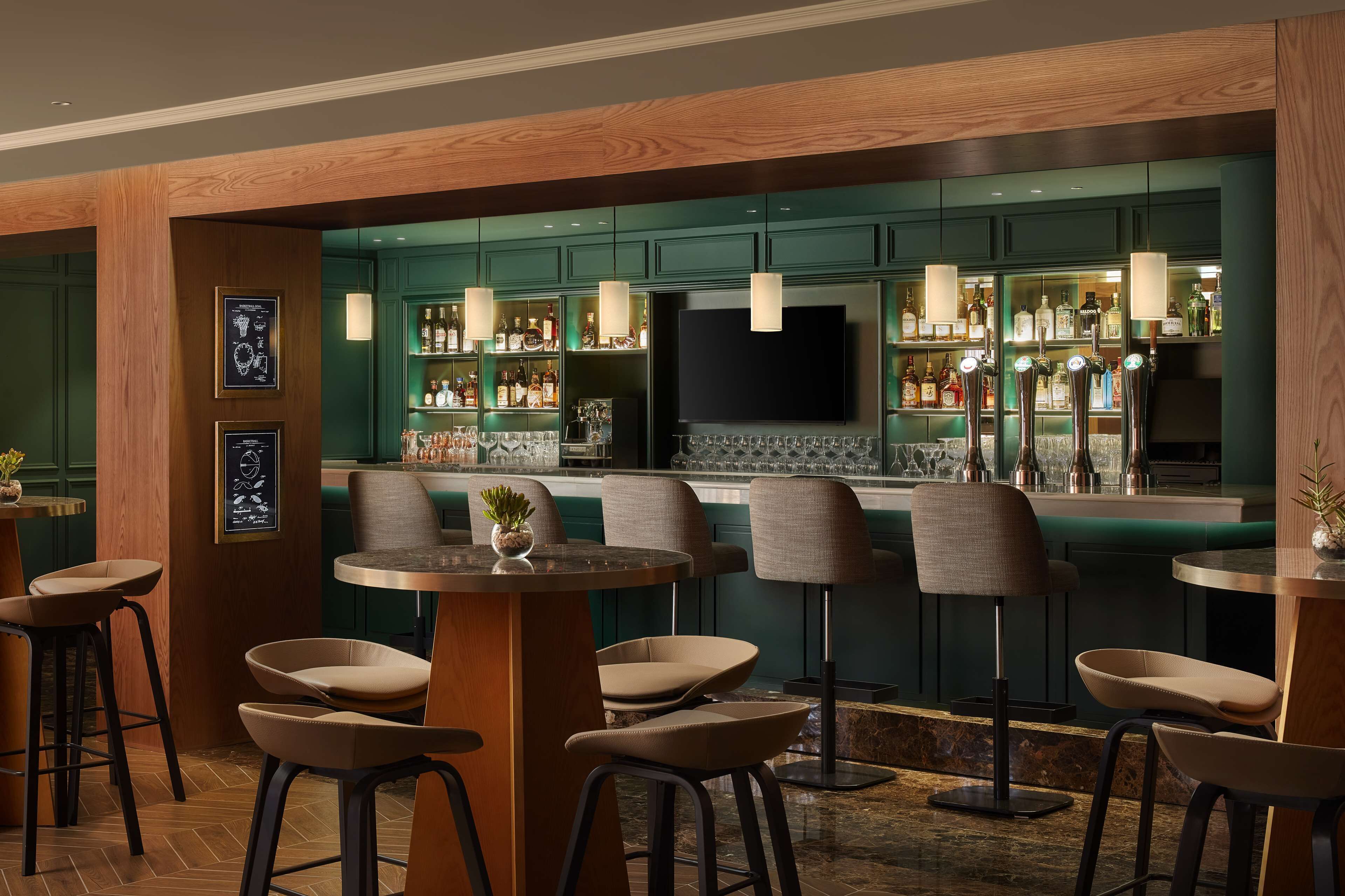 A bar area with high stools, a television, and shelves stocked with bottles.