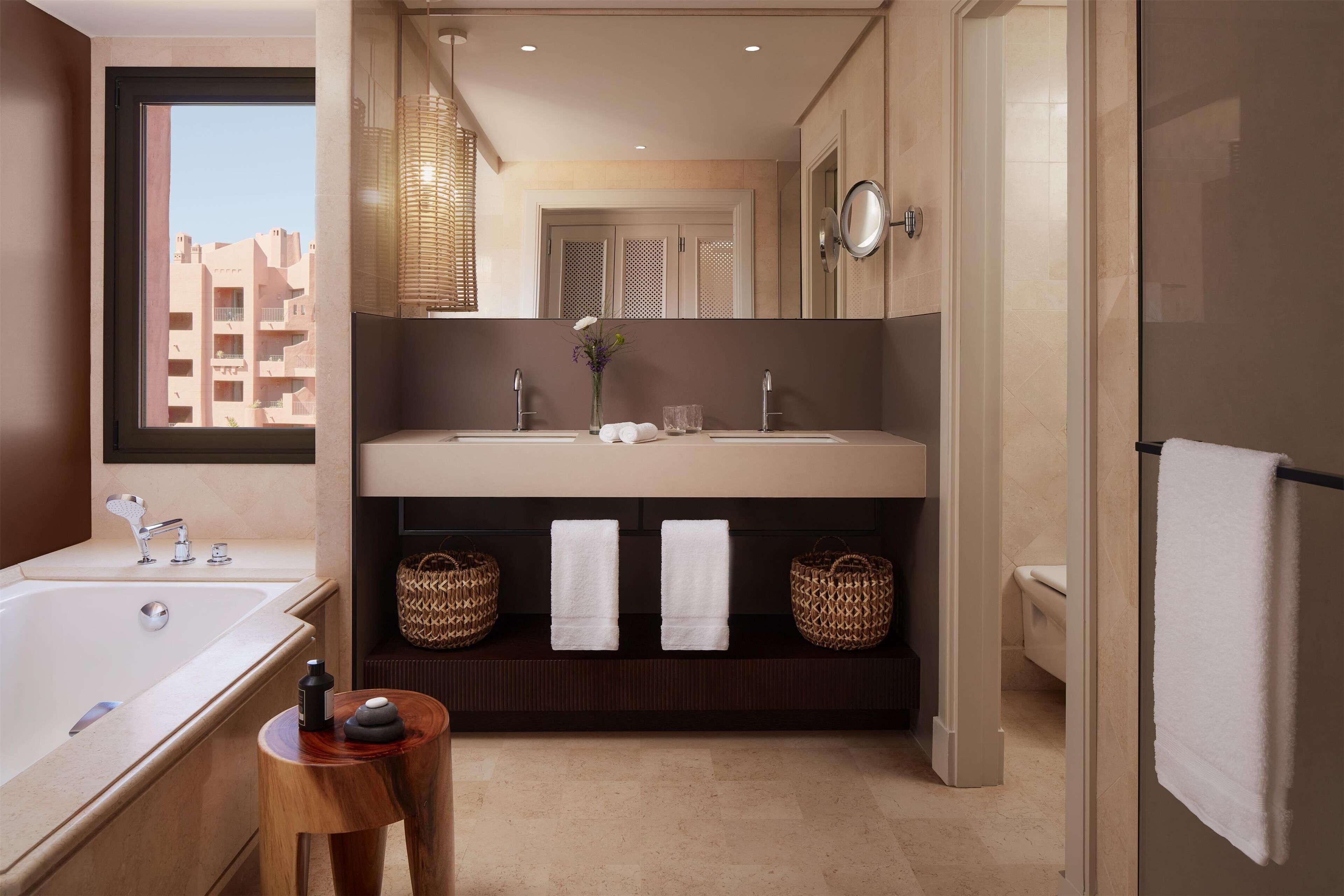 A modern bathroom with a large bathtub, dual sinks, and a vanity with baskets.