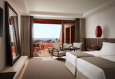 A hotel room with two beds, a balcony with a view, a TV, and a red pendant light.