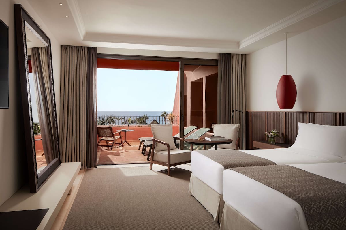 A hotel room with two beds, a balcony with a view, a TV, and a red pendant light.