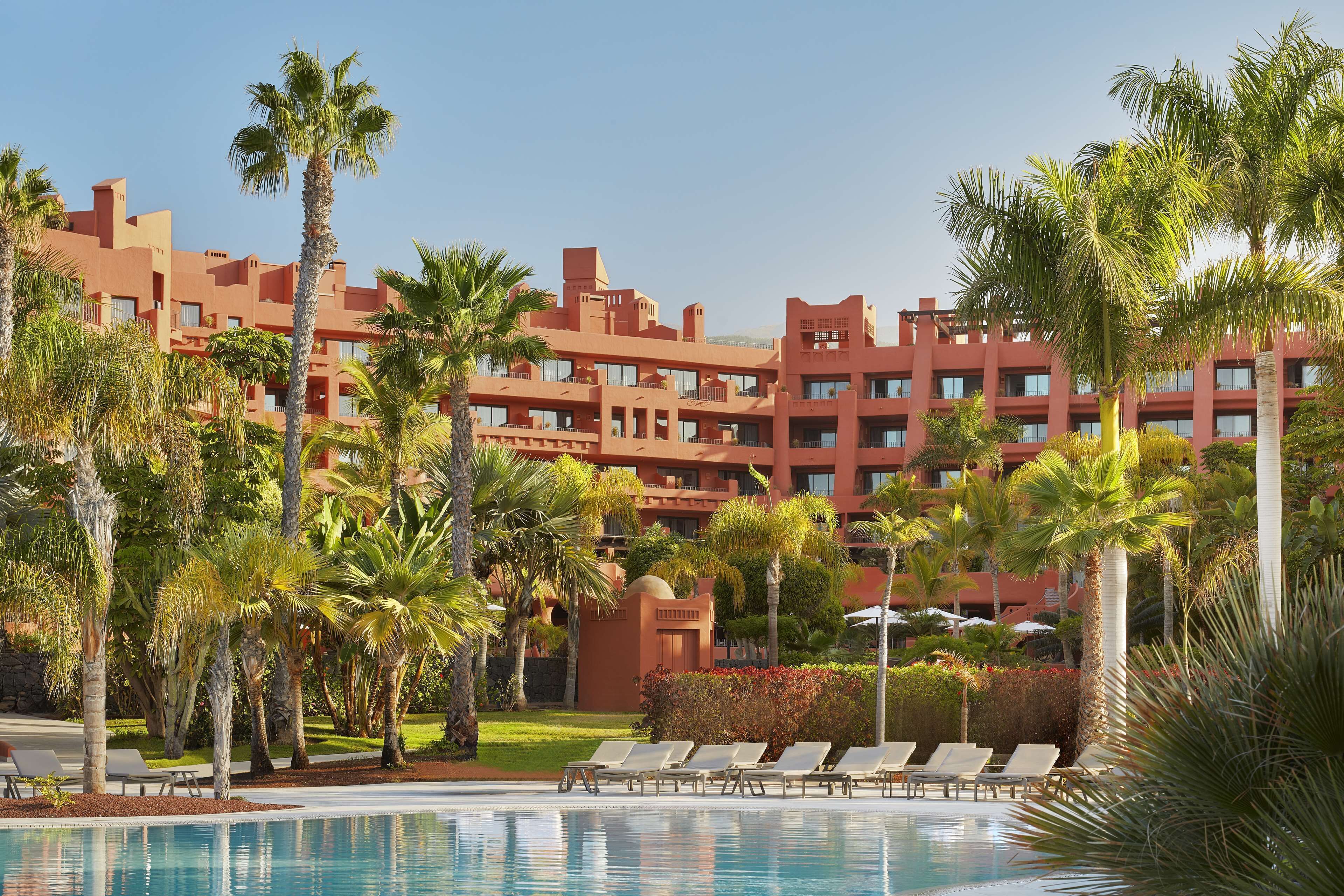 Ein Hotel mit Poolbereich, Palmen und einer roten Gebäudefassade.