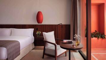 Una habitación de hotel con cama, una silla, una mesita con un florero y un ventanal grande.