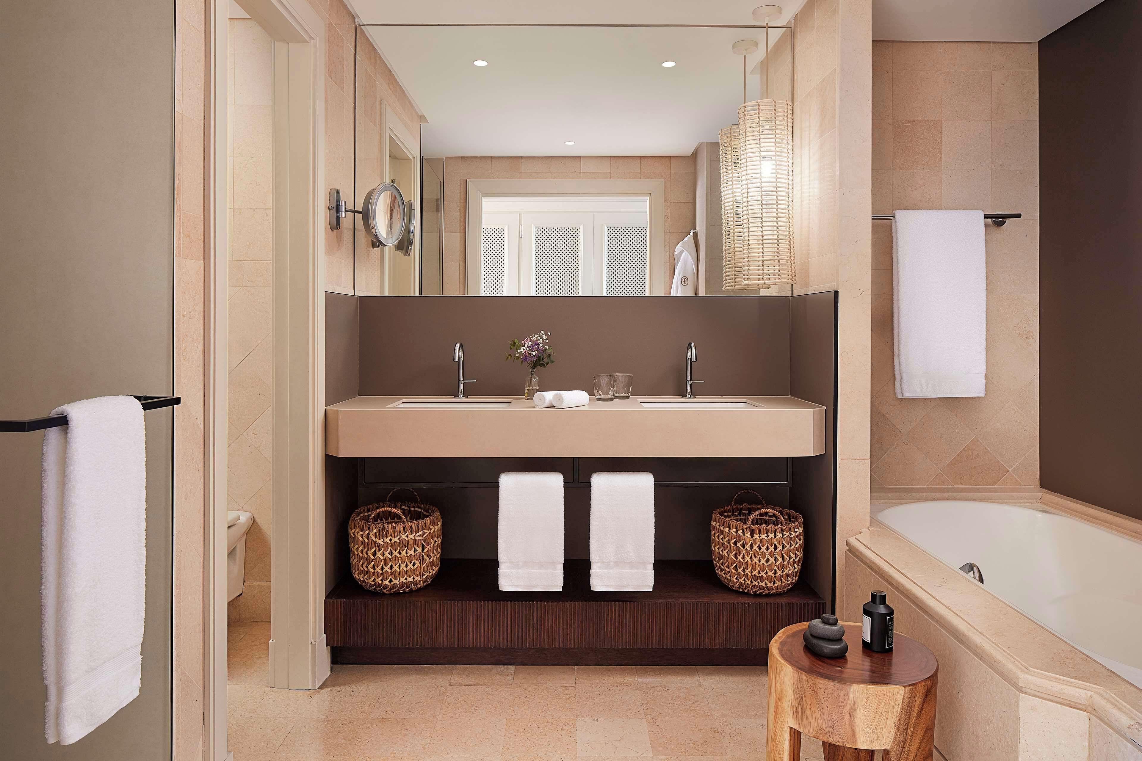A modern bathroom with a large bathtub, a double sink vanity, and two wicker baskets on the floor.