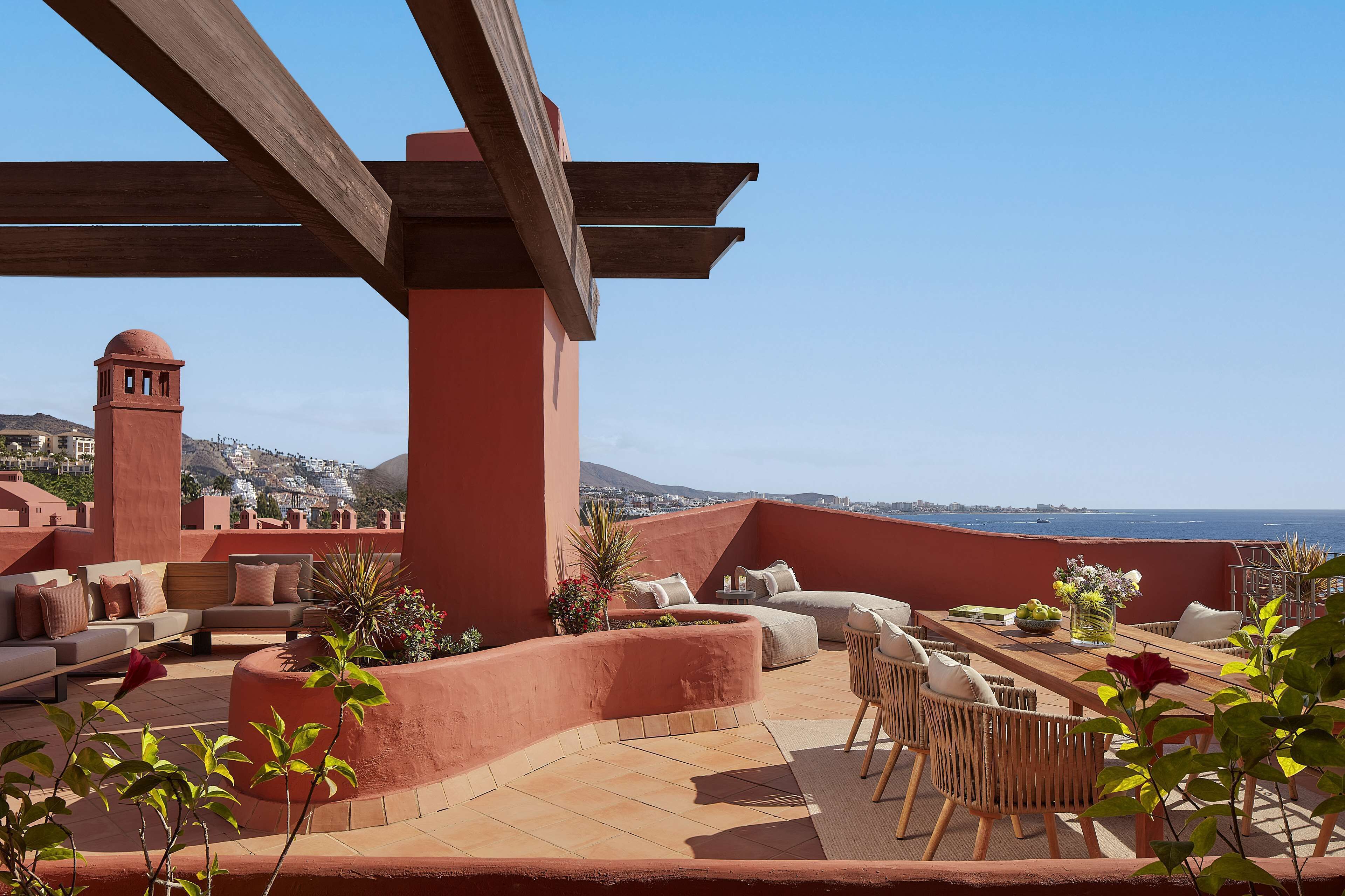 A rooftop terrace with outdoor seating, a view of the city, and a distant mountain range.