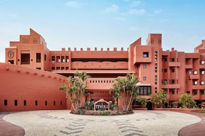 A large, multi-story hotel with a distinctive red facade and a central courtyard with palm trees. - Tivoli la Caleta Resort (Adeje)
