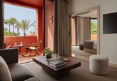 A modern hotel room with a balcony, a sofa, a coffee table, and a view of palm trees.