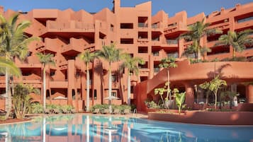 A hotel with a pool, palm trees, and a red building facade.