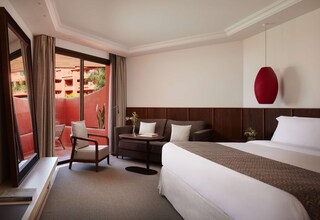 A hotel room with a bed, a desk, a chair, a small table, and a large window.