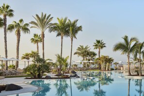 A pool area with palm trees, lounge chairs, and umbrellas. - Tivoli la Caleta Resort (Adeje)