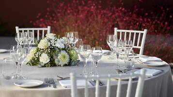 Una mesa redonda dispuesta con sillas blancas, cristalería transparente y un centro de mesa floral.