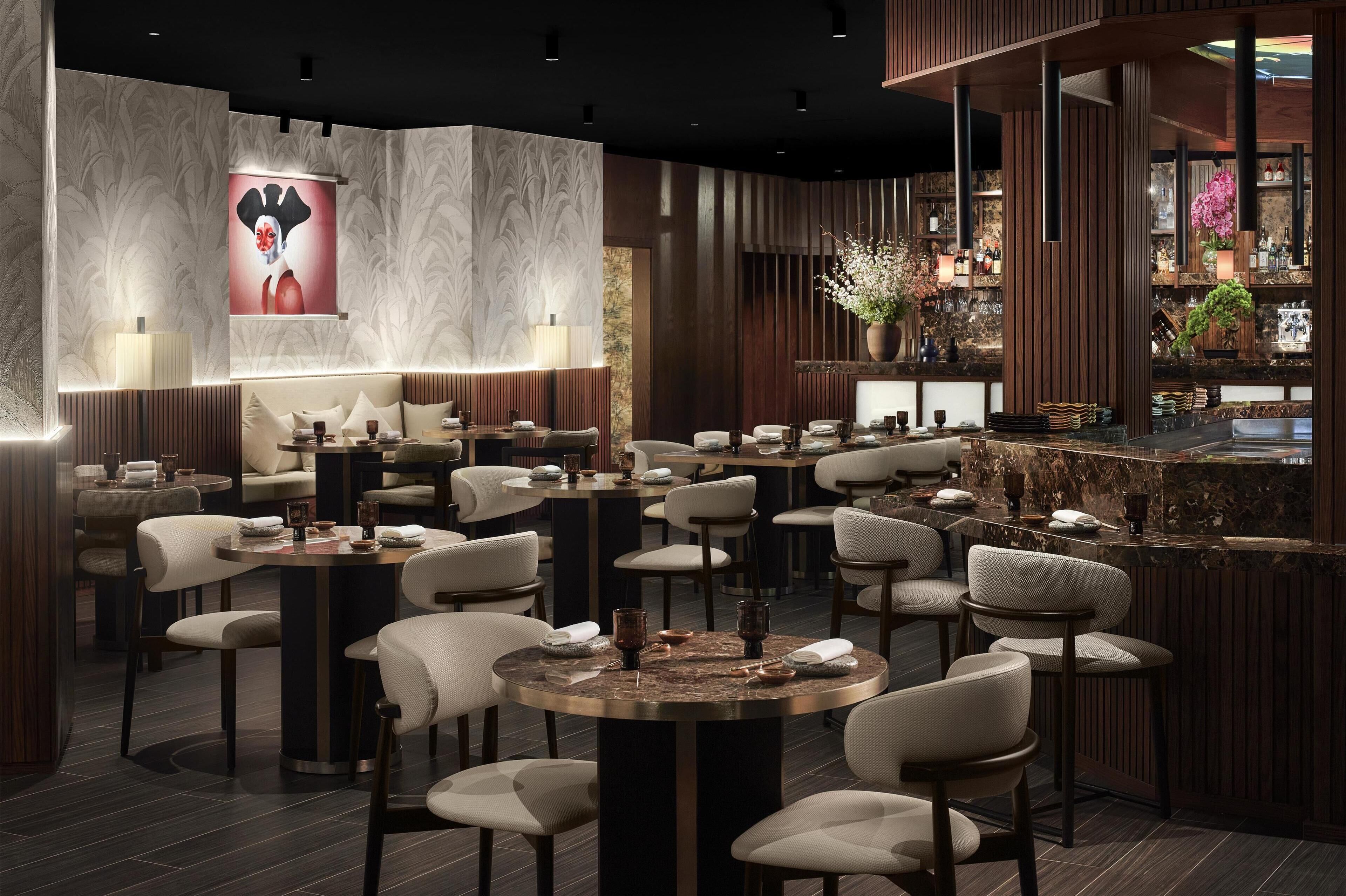 Eine moderne Bar mit runden Tischen und Barhocker, einer großen beleuchteten Kunstinstallation und einer Bar Theke mit verschiedenen Gegenständen und Pflanzen.