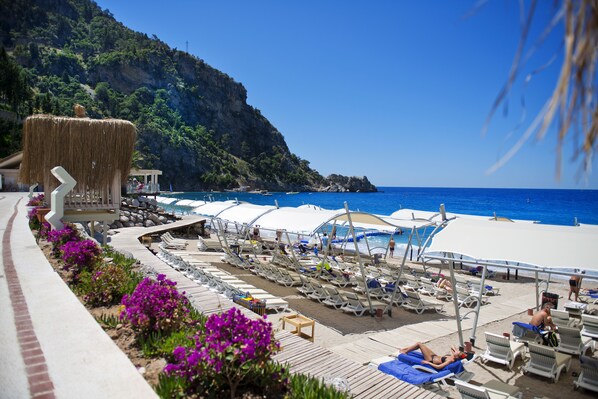 Un resort sul lungomare con lettini, una piscina e una struttura con tetto di paglia.