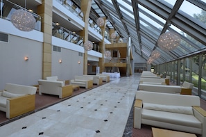 A spacious indoor area with multiple levels, featuring a central walkway, seating areas, and hanging spherical light fixtures.