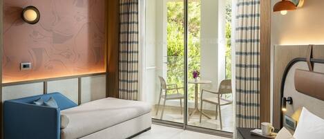 A hotel room with a bed, a sofa, a small table with a chair, a nightstand, and a sliding glass door leading to an outdoor area with a table and chairs.