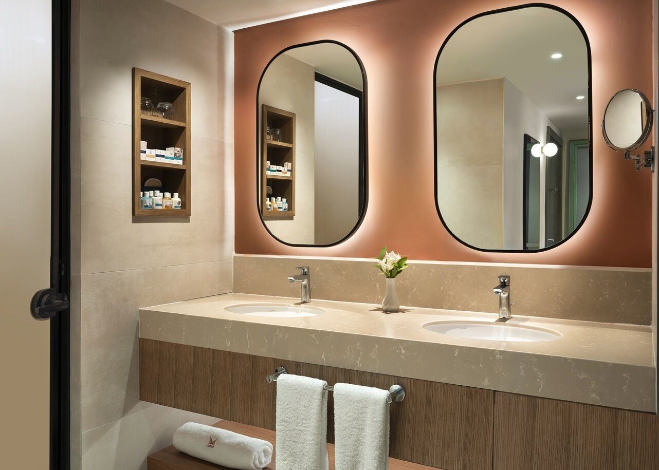 A modern bathroom with two sinks, a large mirror, and a shelf with toiletries.