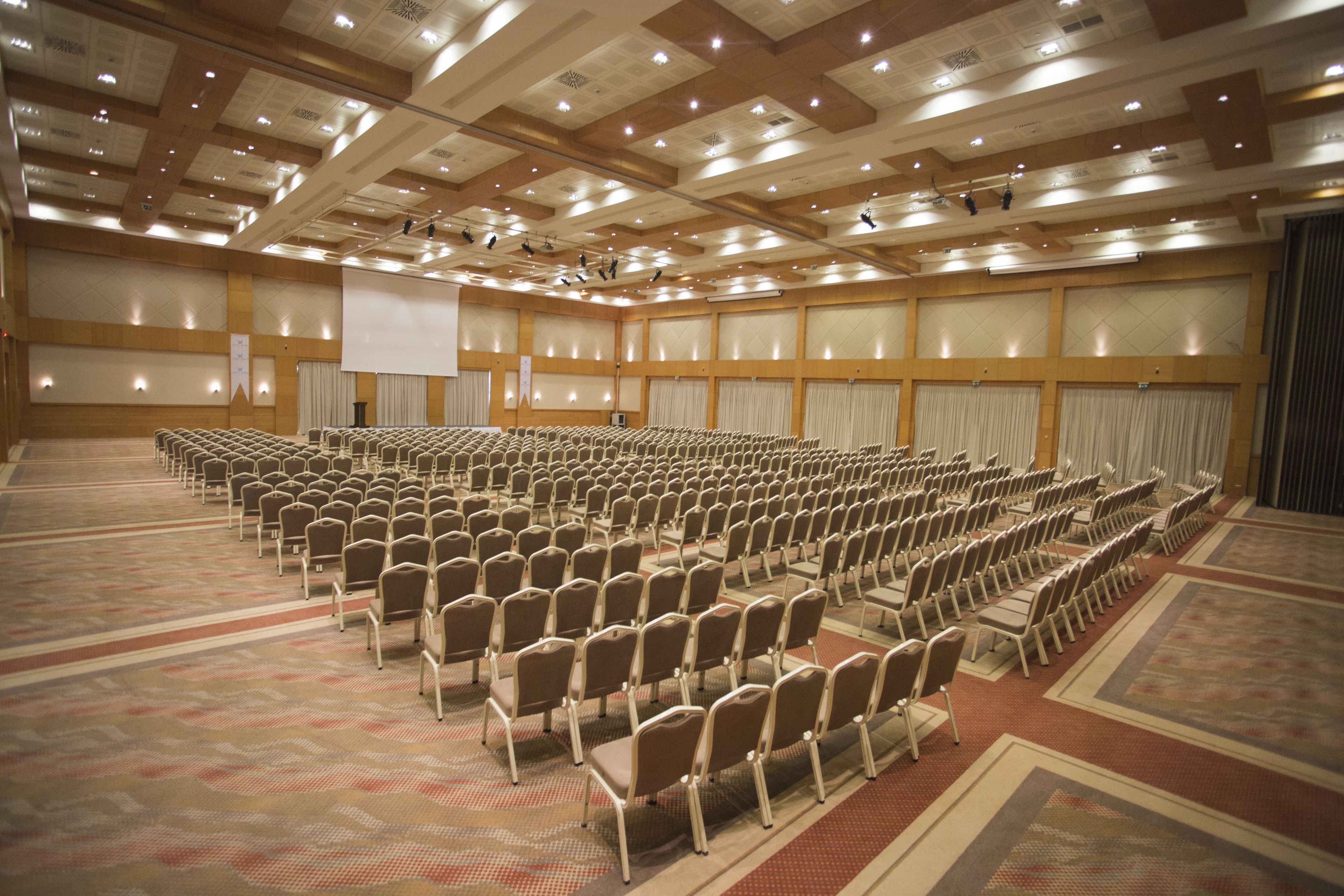 A large conference room with rows of chairs, a stage with a screen, and a carpeted floor.