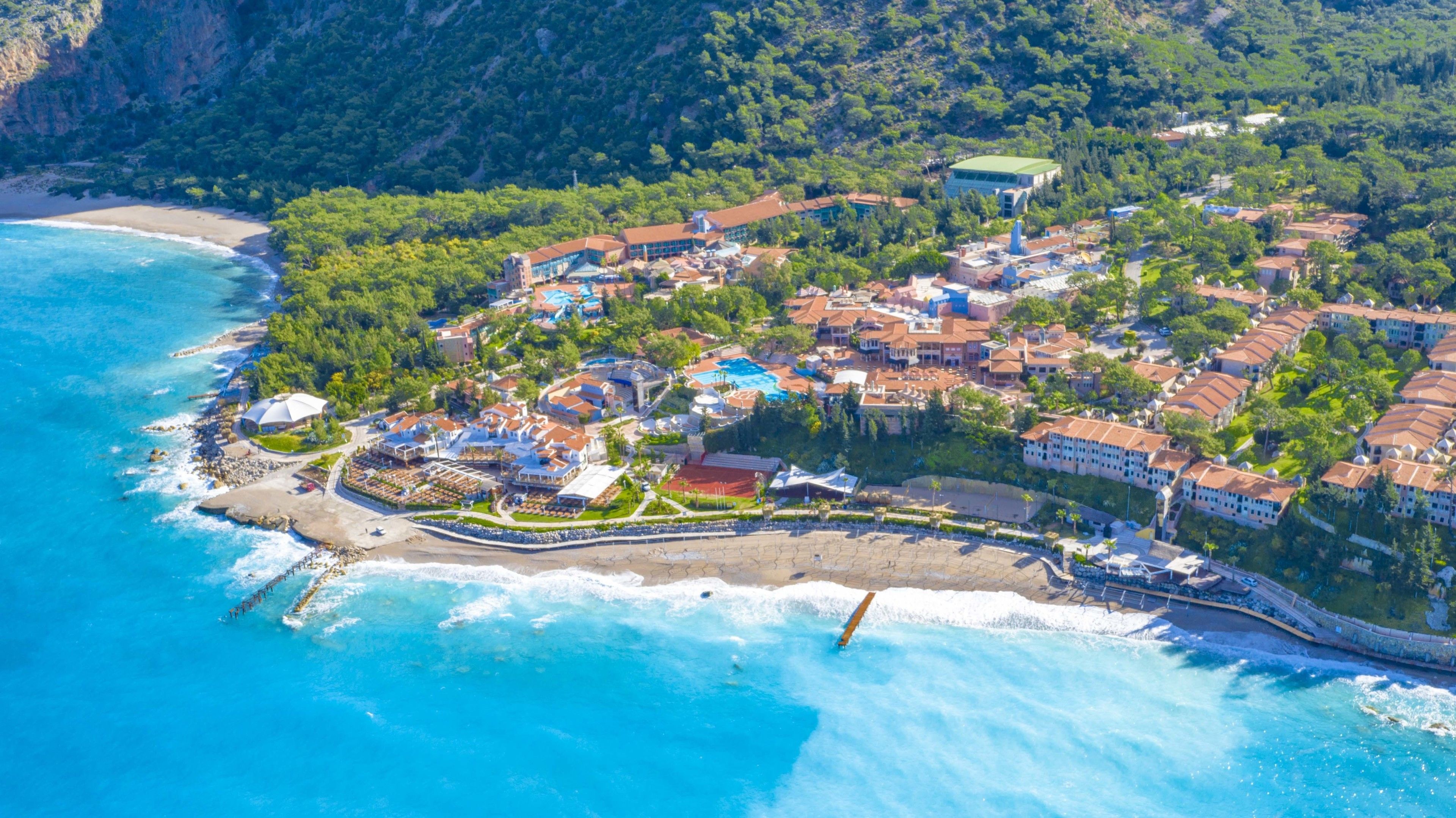 An aerial view of a coastal resort with a beach, villas, and a pool area.