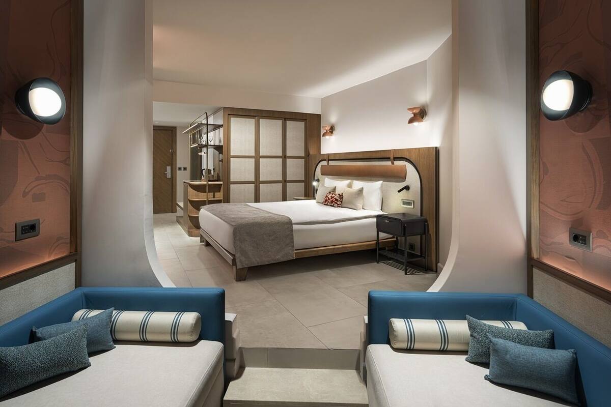 A modern hotel room with a large bed, a desk, and two sofas.