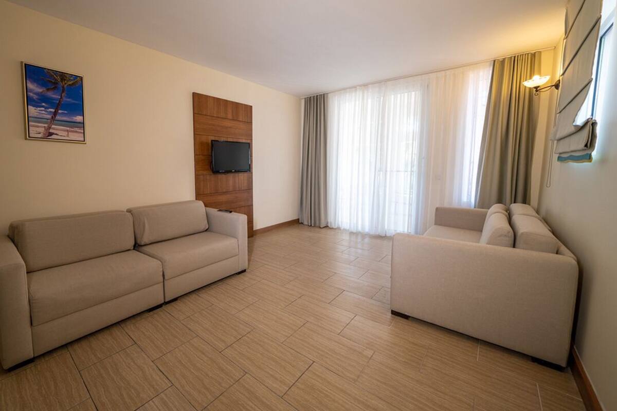 A living room with two sofas, a flat-screen TV, and a large window with curtains.