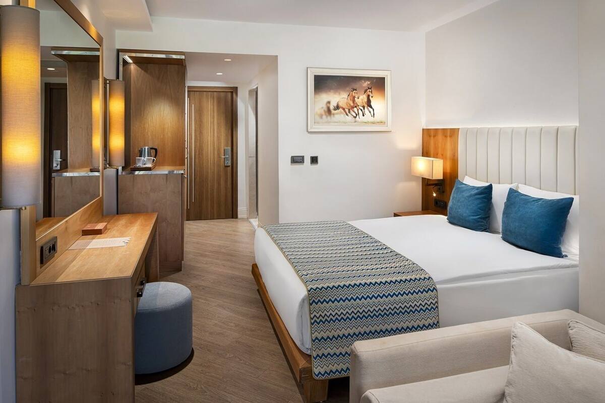 A hotel room with a bed, a desk, a chair, a mirror, and a painting on the wall.