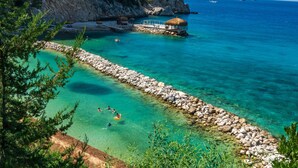 A coastal area with clear turquoise water, a rocky shoreline, and a small building with a thatched roof near the water's edge. - Liberty Lykia (Fethiye)
