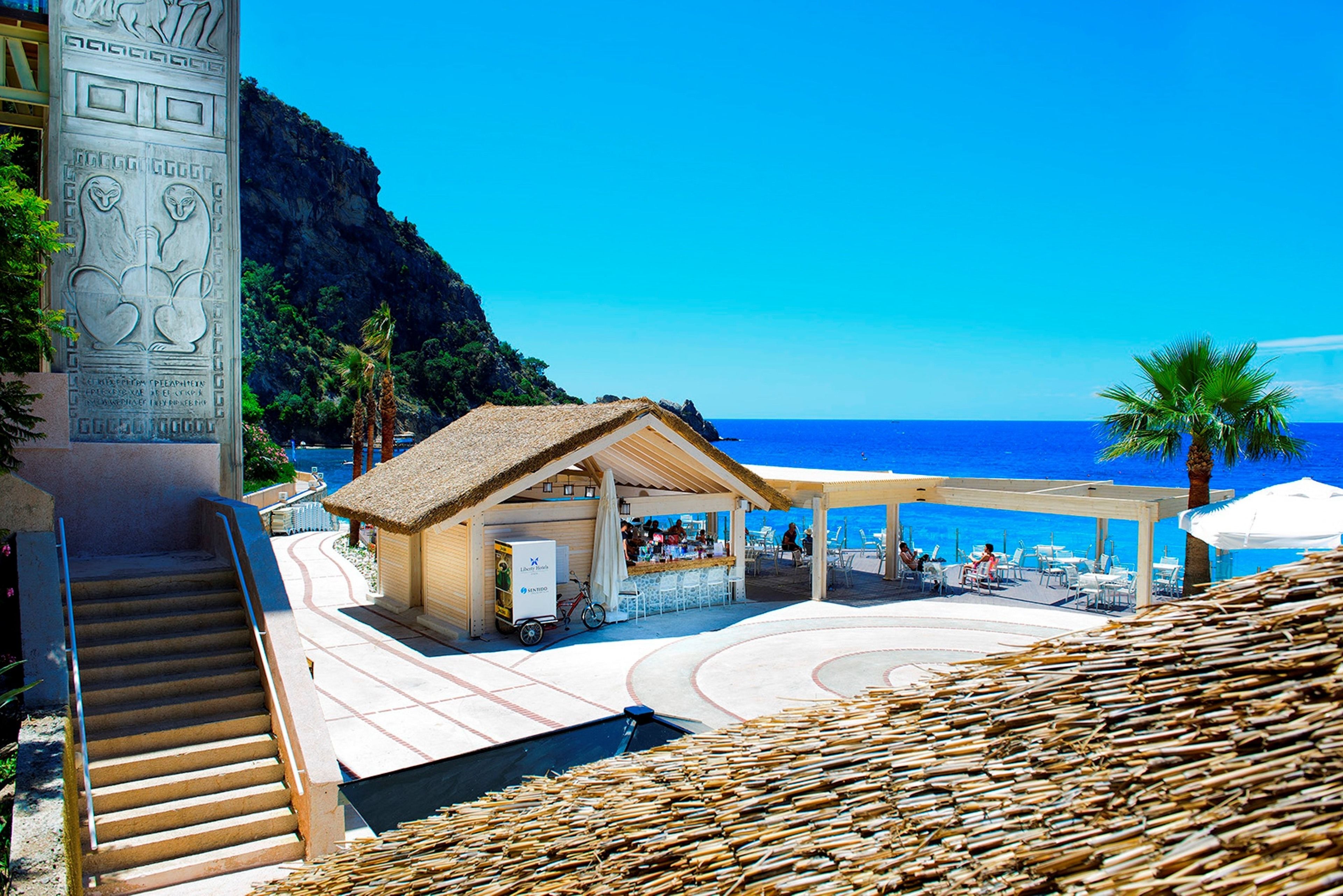 Un resort frente al mar con un bar de techo de paja, asientos al aire libre y vista al océano.