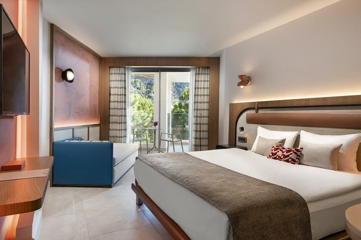 A hotel room with a bed, a desk, a chair, and a TV.