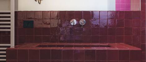 Un baño con un lavamanos de azulejos rojos, un espejo y un perchero para toallas.