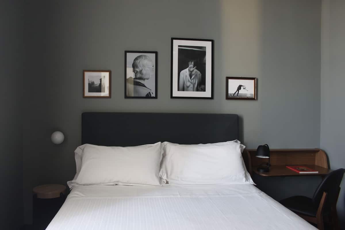 A hotel room with a bed, a nightstand, a desk with a chair, and three framed pictures on the wall.