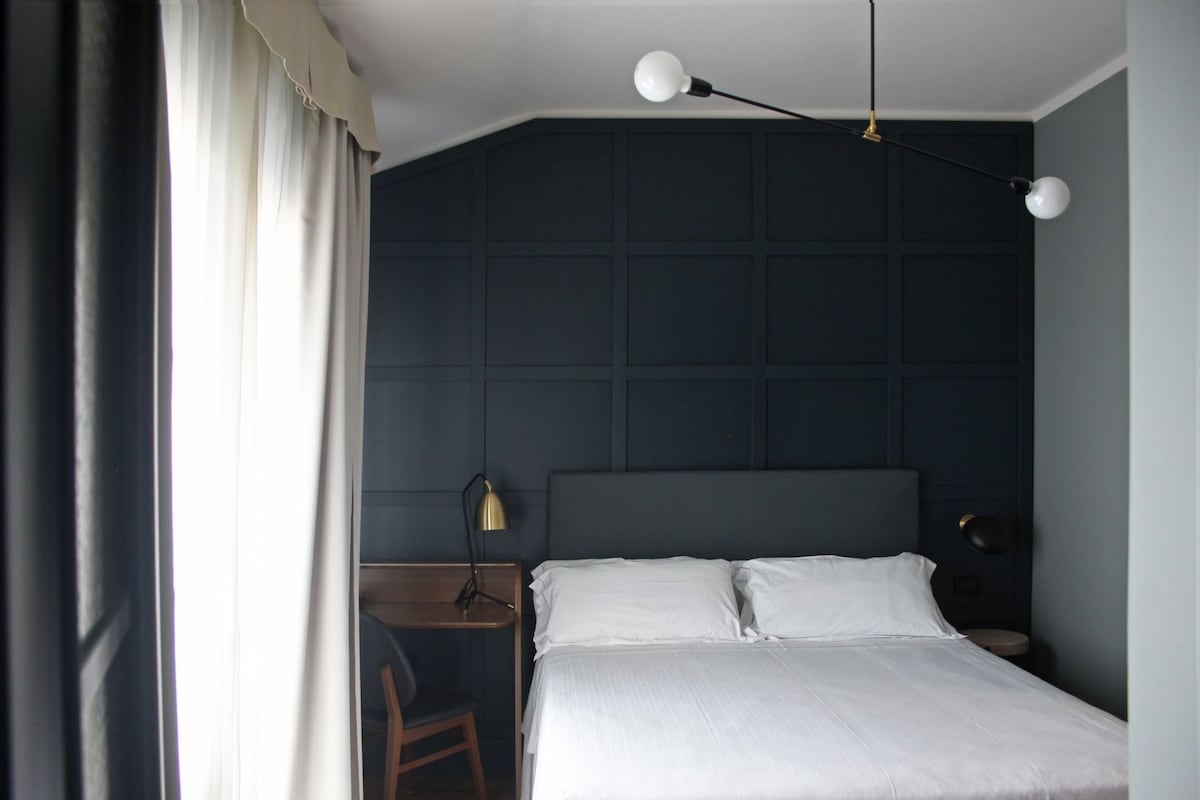 A bedroom with a bed, a desk, a chair, a lamp, and a dark wall.