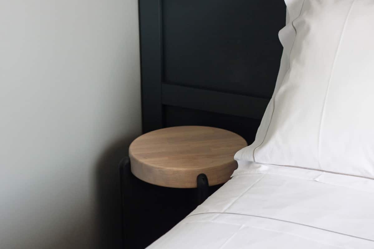 A bed with white bedding and a wooden bedside table.