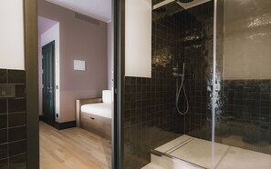 A modern bathroom with a glass shower enclosure, a wooden floor, and a bed in the adjacent room. - c-hotels Diplomat (Florence)