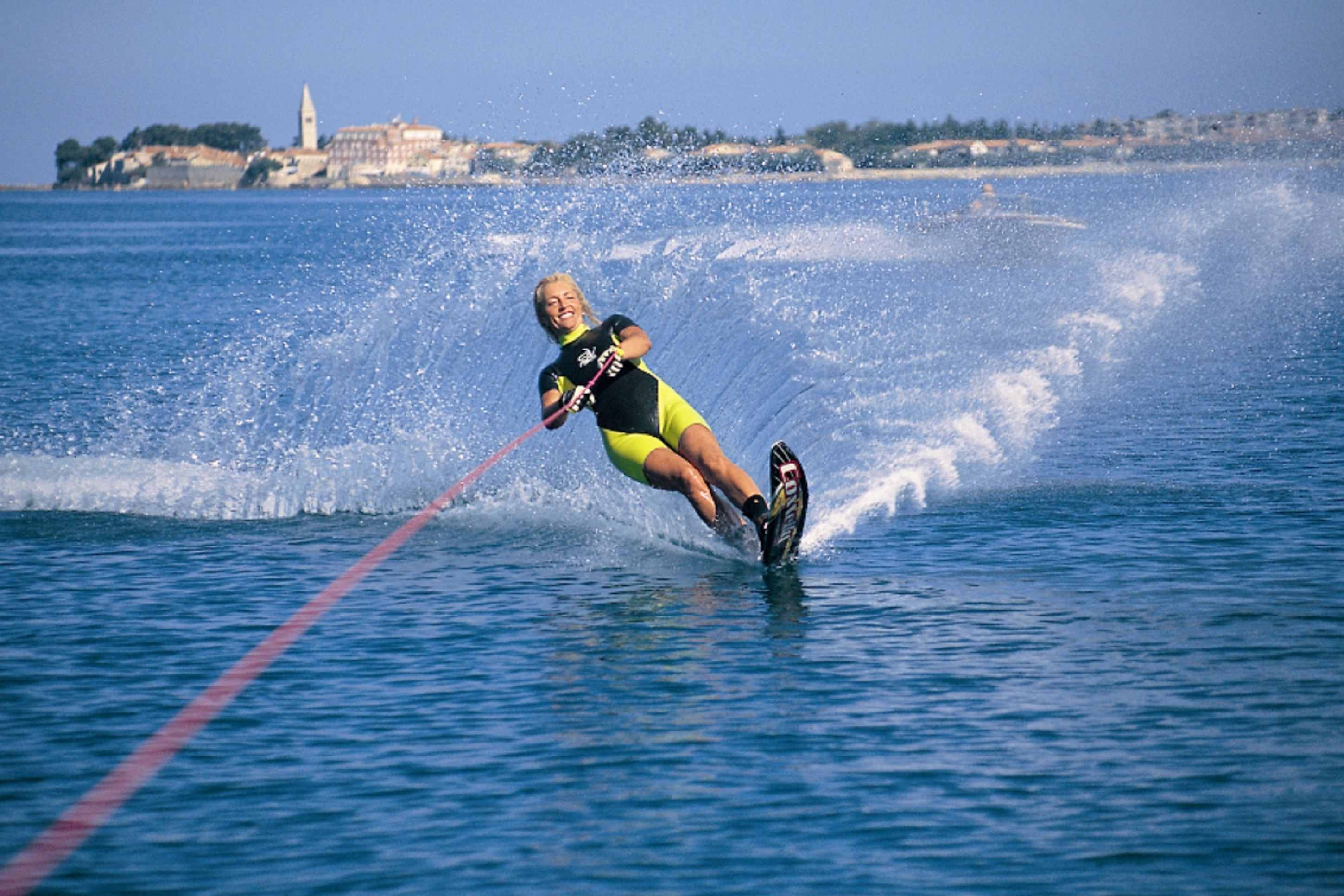 Une personne fait du wakeboard sur une étendue d’eau, tirée par un câble rouge.
