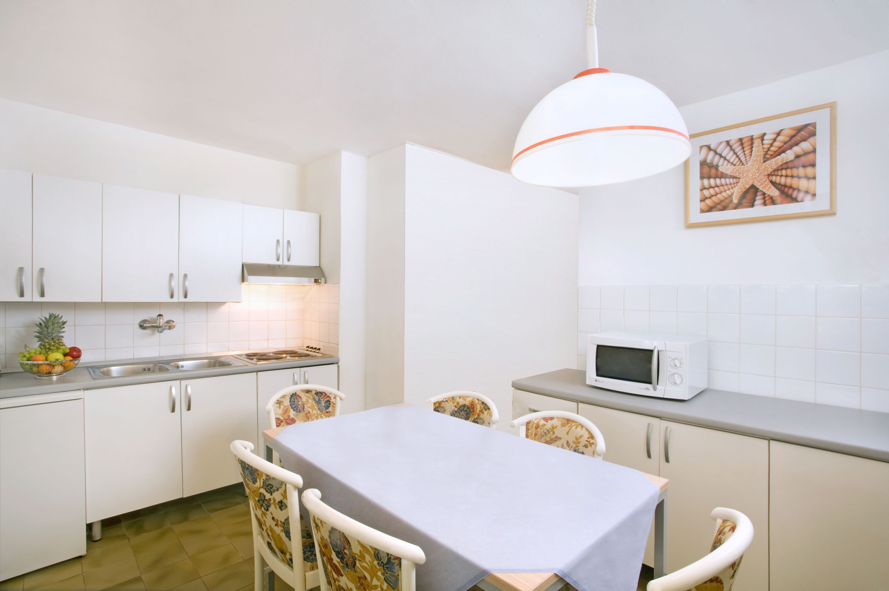 A kitchen with white cabinets, a dining table with chairs, a microwave, and a fruit bowl.