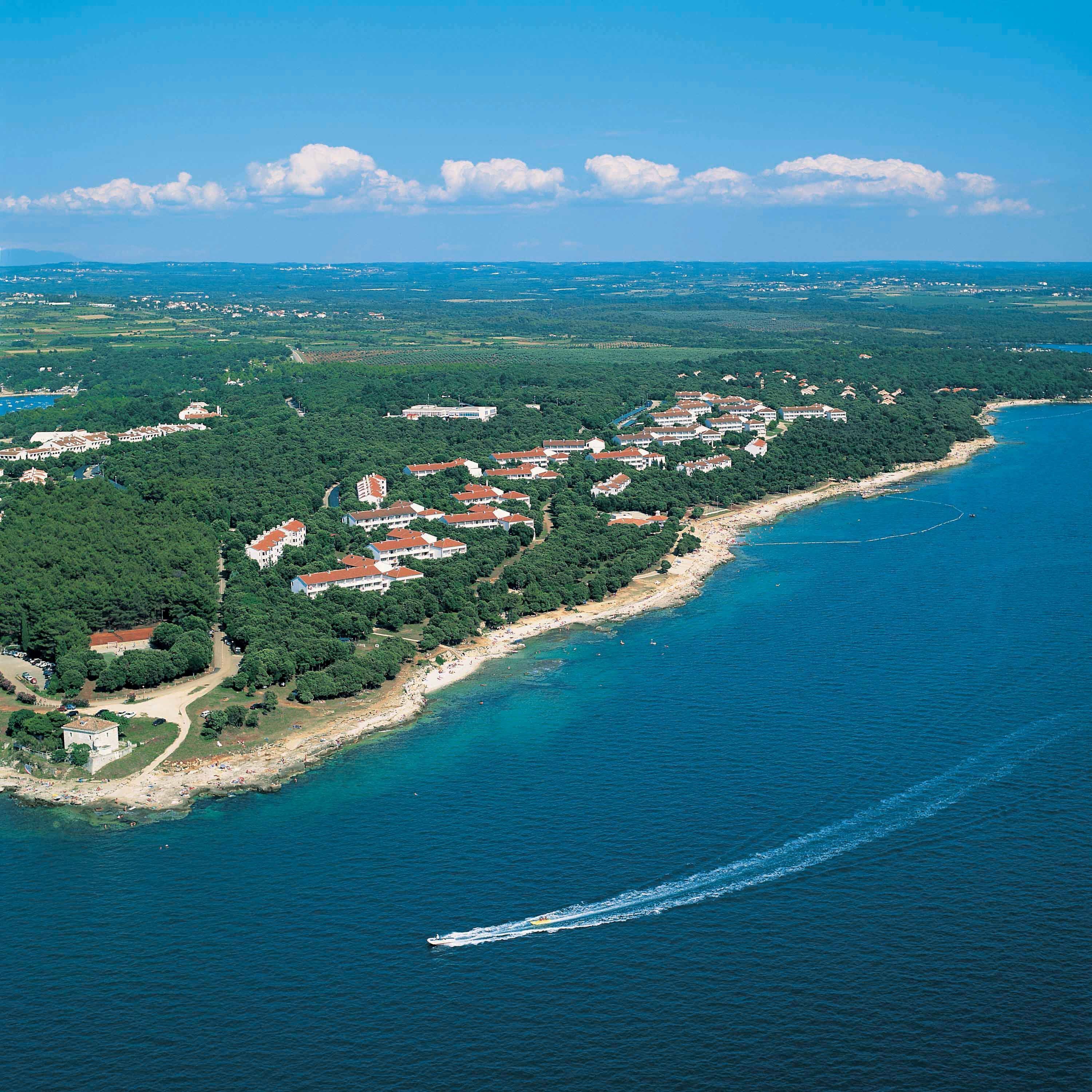 An aerial view of a coastal resort with multiple buildings, a beach, and a clear blue sea.