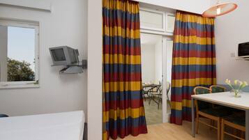 Una habitación con una cama, un escritorio con una silla, un televisor en un estante y una ventana con cortinas.