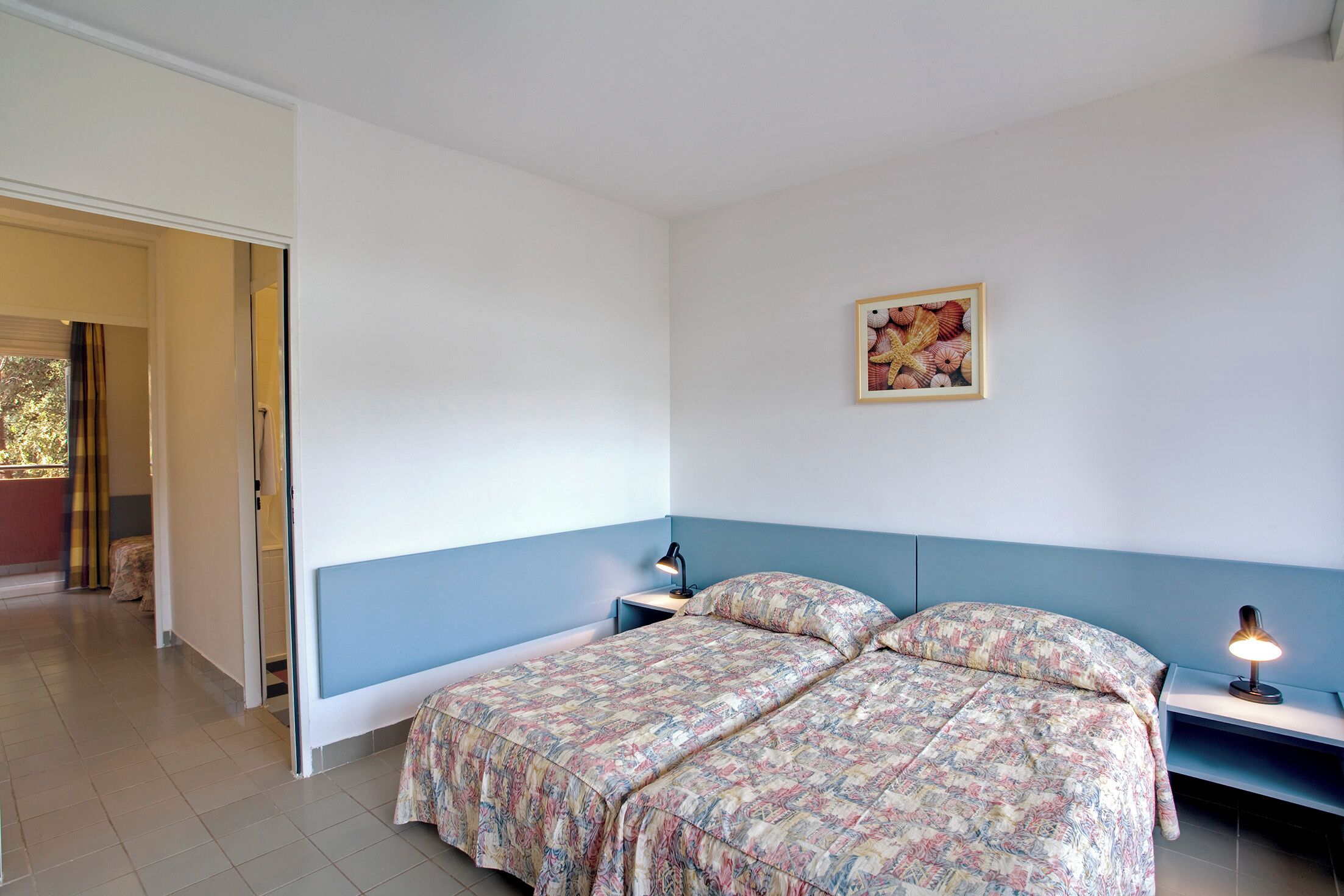 A bedroom with a bed, two bedside tables, a lamp on each table, and a framed picture on the wall.