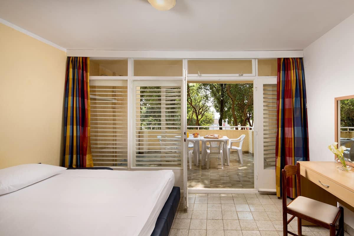 A hotel room with a bed, a desk, and a view of an outdoor patio with a table and chairs.